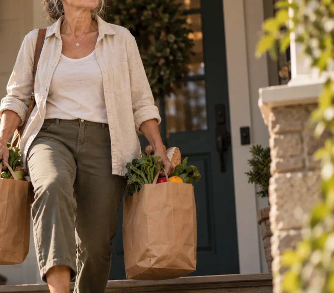 A woman carrying two grocery bags down the steps of her home